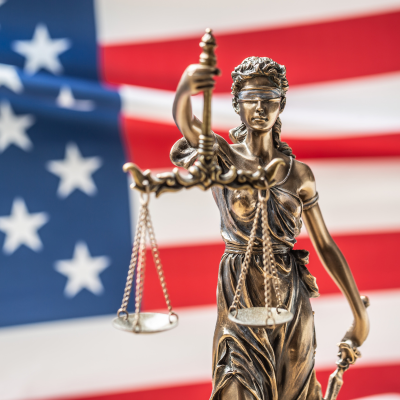 A bronze statue of the Lady of Justice with a blind fold holding scales stands in front of the American flag