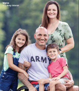 U.S. Army Veteran Marco poses in his wheelchair with his wife behind him and his children on either side.