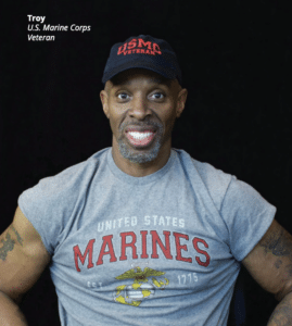 Troy, U.S. Marine Corps Veteran, smiles for the camera against a black background.