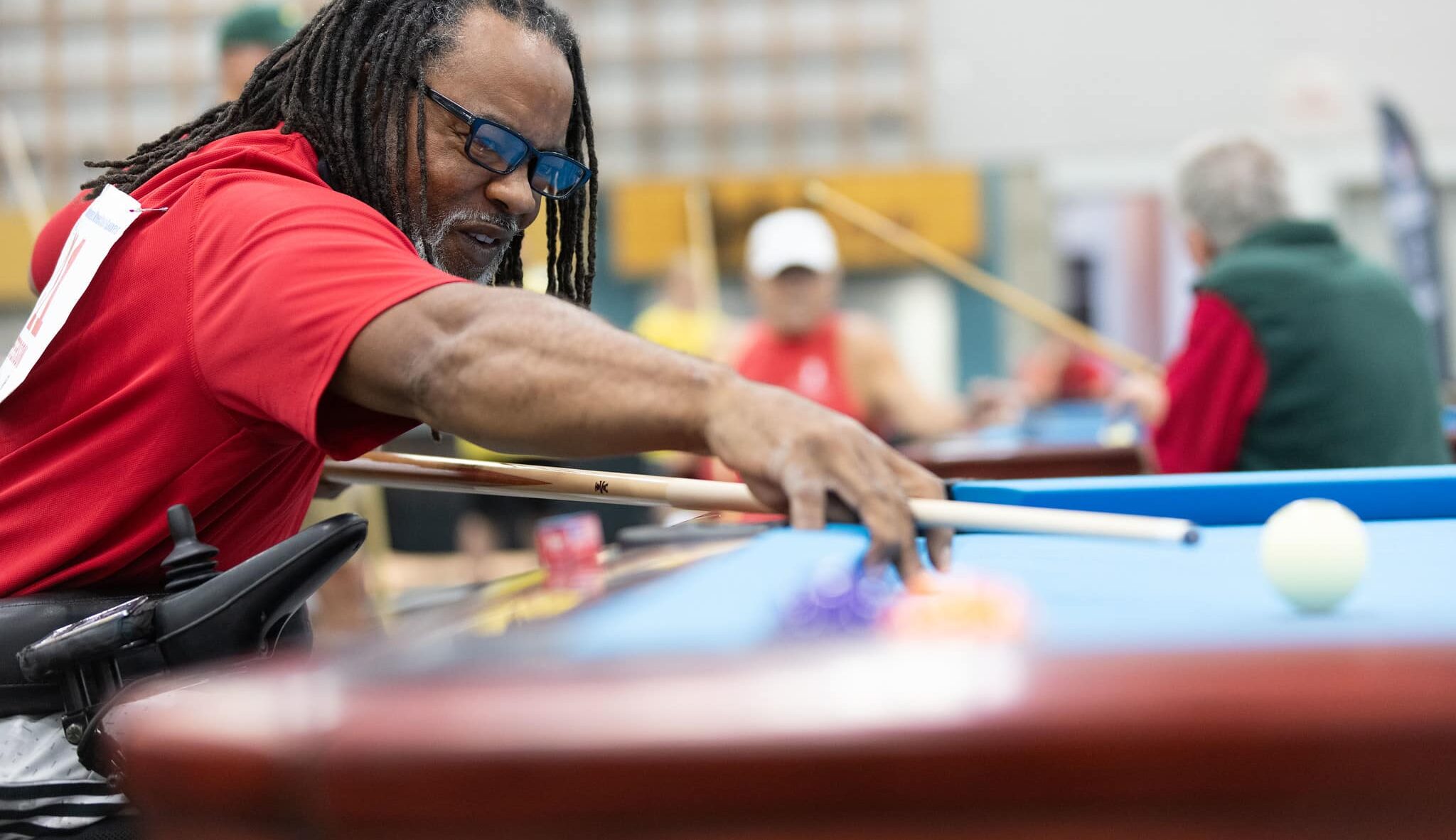 A man in a wheelchair lines up his shot at a billiards table
