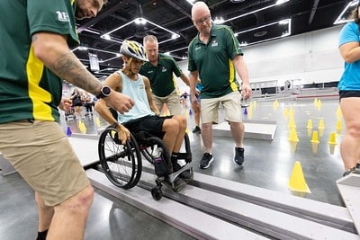Volunteers help guide a wheelchair slalom participant through the course at the 2023 wheelchair games.