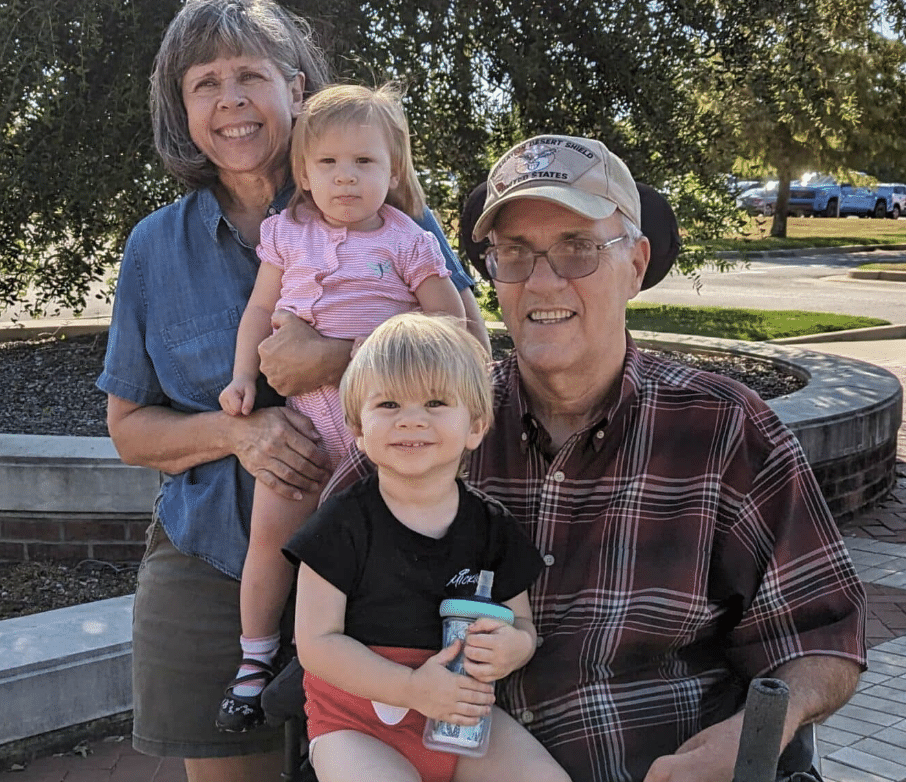 Two smiling grandparents with two small children.