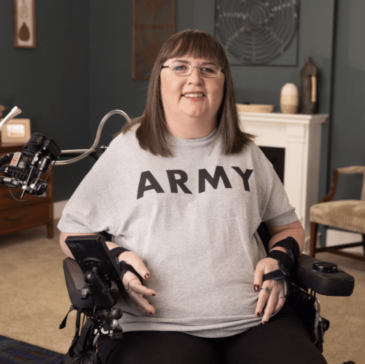 U.S. Army Veteran Anne smiles at the camera. She wears glasses and is in a power wheelchair.