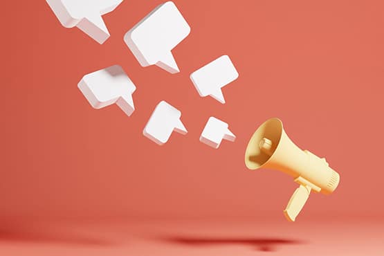 A yellow megaphone emits several floating white speech bubbles against a plain, coral-colored background, symbolizing communication or spreading messages.