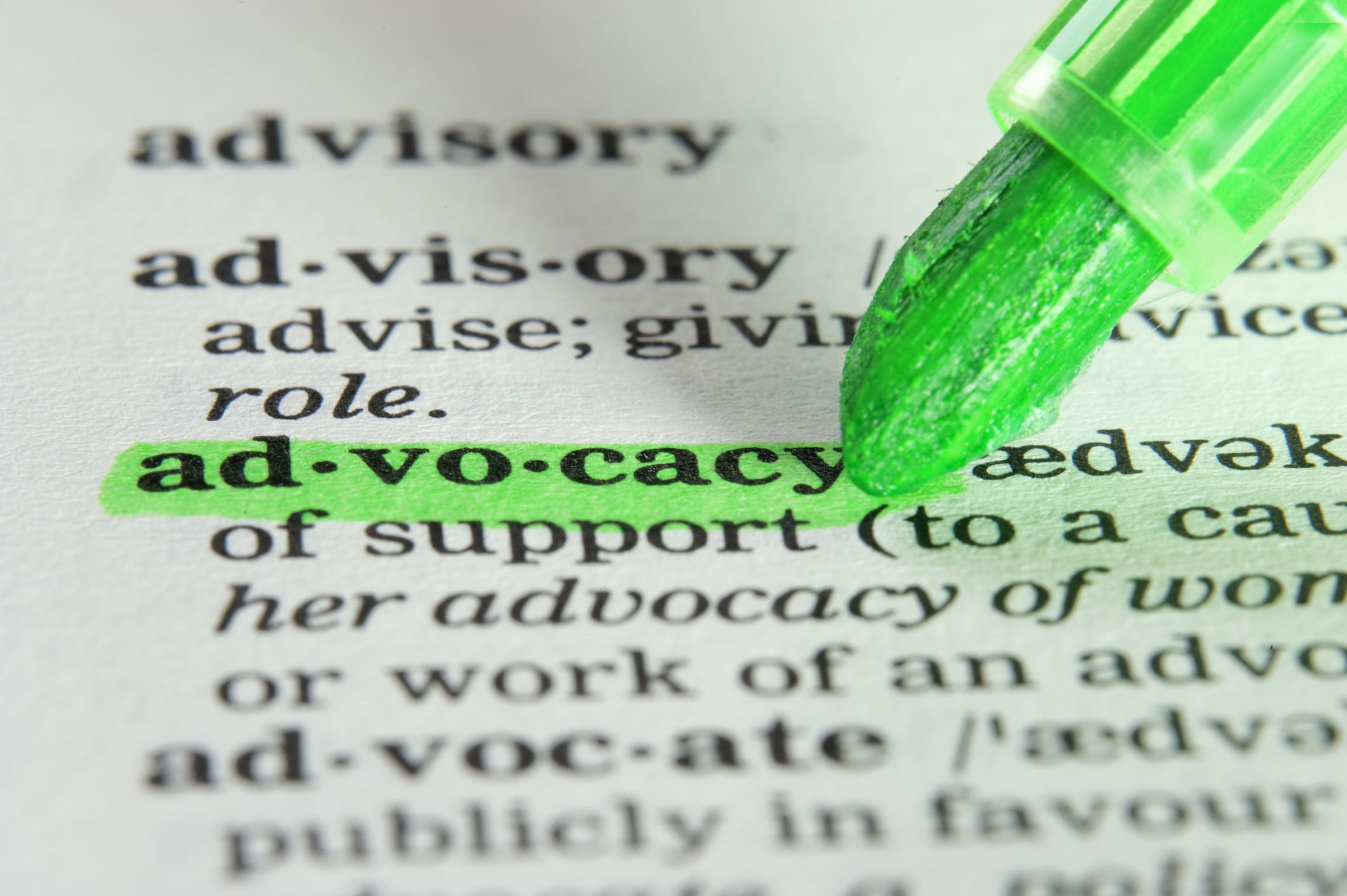 A green highlighter marks the word "advocacy" in a dictionary, with the definition partially visible around the highlighted text.