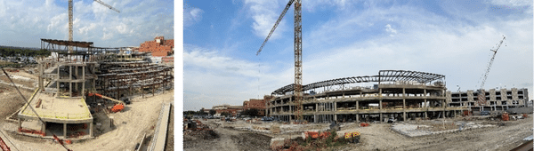 Panoramic view of a large construction site with multiple cranes, partially built multi-story buildings, and construction equipment scattered around under a partly cloudy sky.
