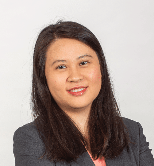 Manrui Zhang, a woman with straight, dark brown hair wearing a gray blazer and a coral top smiles at the camera against a plain white background.