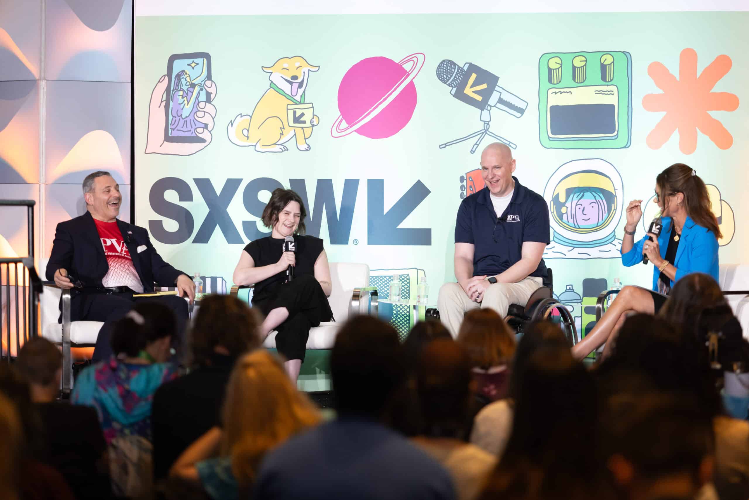 Four people sit on stage speaking at a SXSW panel. Behind them is a colorful backdrop with illustrations and the SXSW logo. The audience sits in the foreground, listening to the discussion.