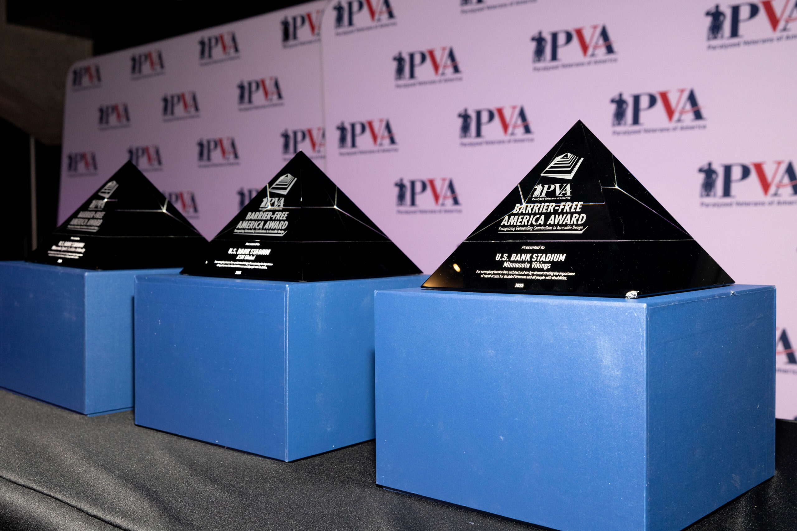 Three black pyramid-shaped awards on blue bases are displayed side by side, with a PVA Step-Free America Award logo, in front of a backdrop featuring repeated PVA logos and branding.